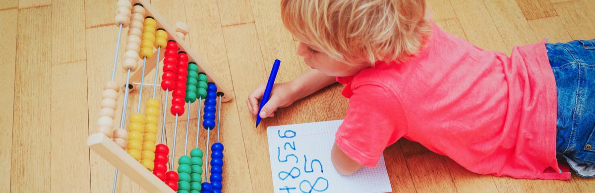 Kind liegt vor Abakus und schreibt Zahlen auf Papier